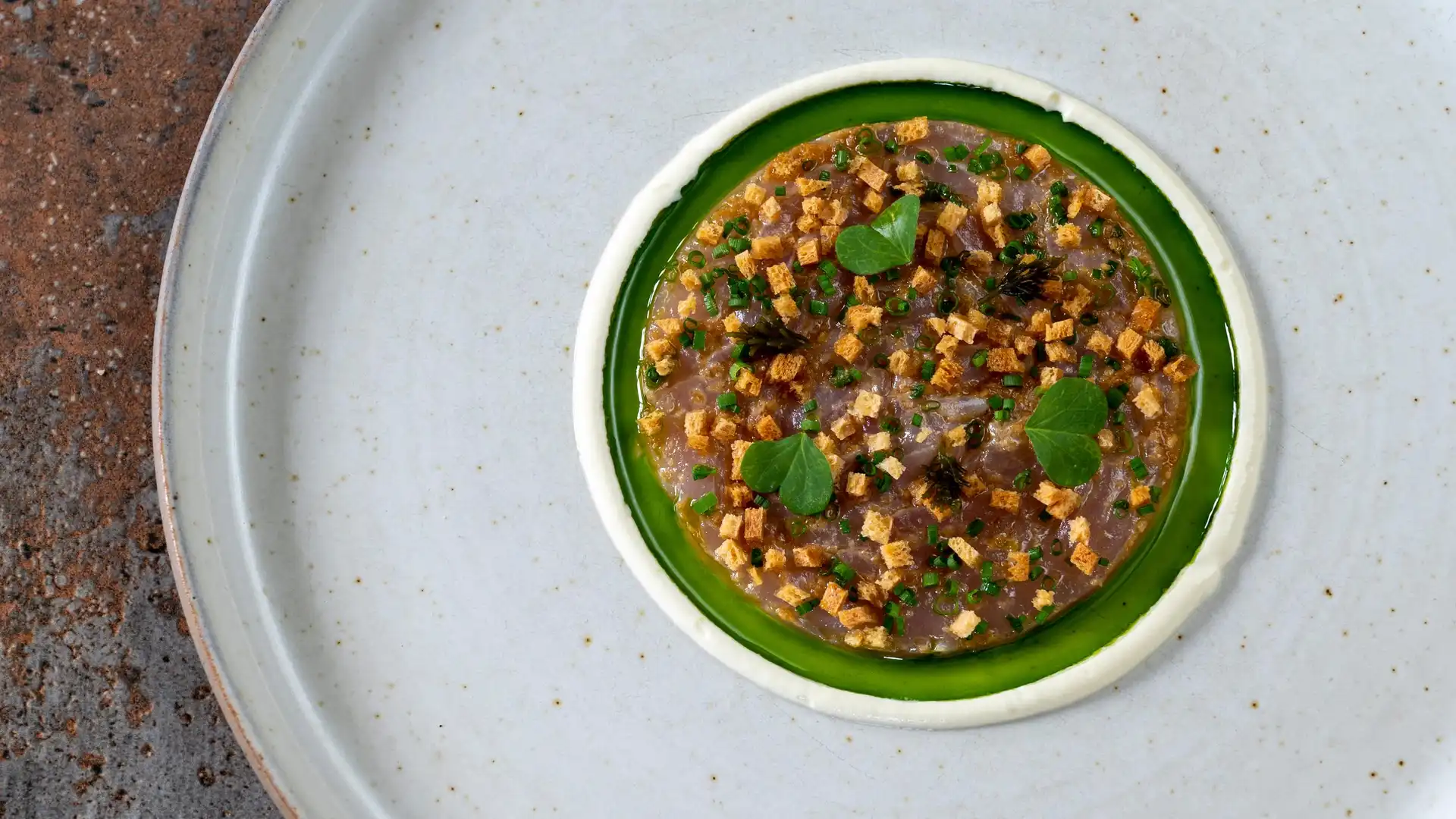 Un petit bol vert contenant un mélange de petits cubes dorés et de feuilles vertes, posé sur une assiette blanche