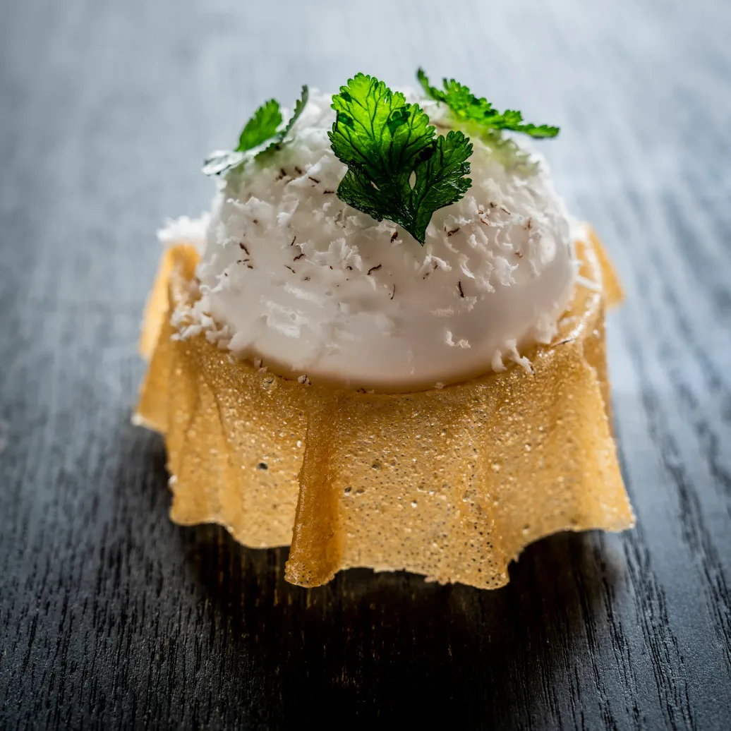Petite pâtisserie garnie de crème blanche saupoudrée de copeaux et décorée de feuilles de céleri sur une base dorée