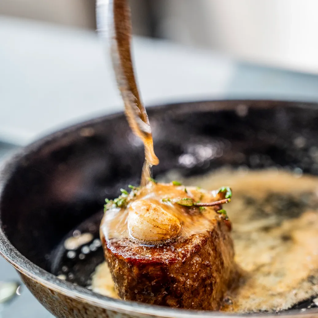 Un morceau de viande cuit dans une poêle avec une sauce au beurre et des herbes