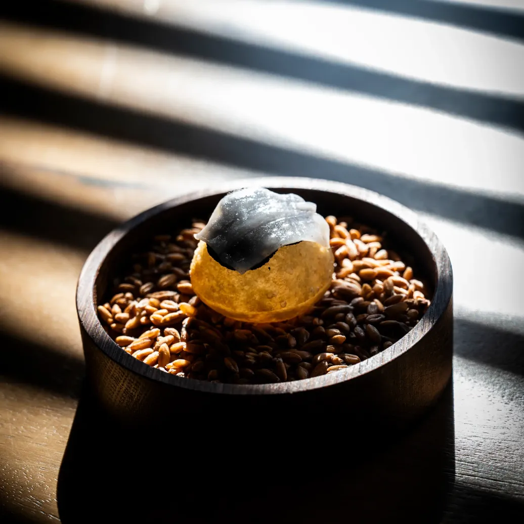 Un bol en bois contenant des graines et un dessert glacé à base de pâte et de charbon actif, éclairé par la lumière du soleil traversant des stores