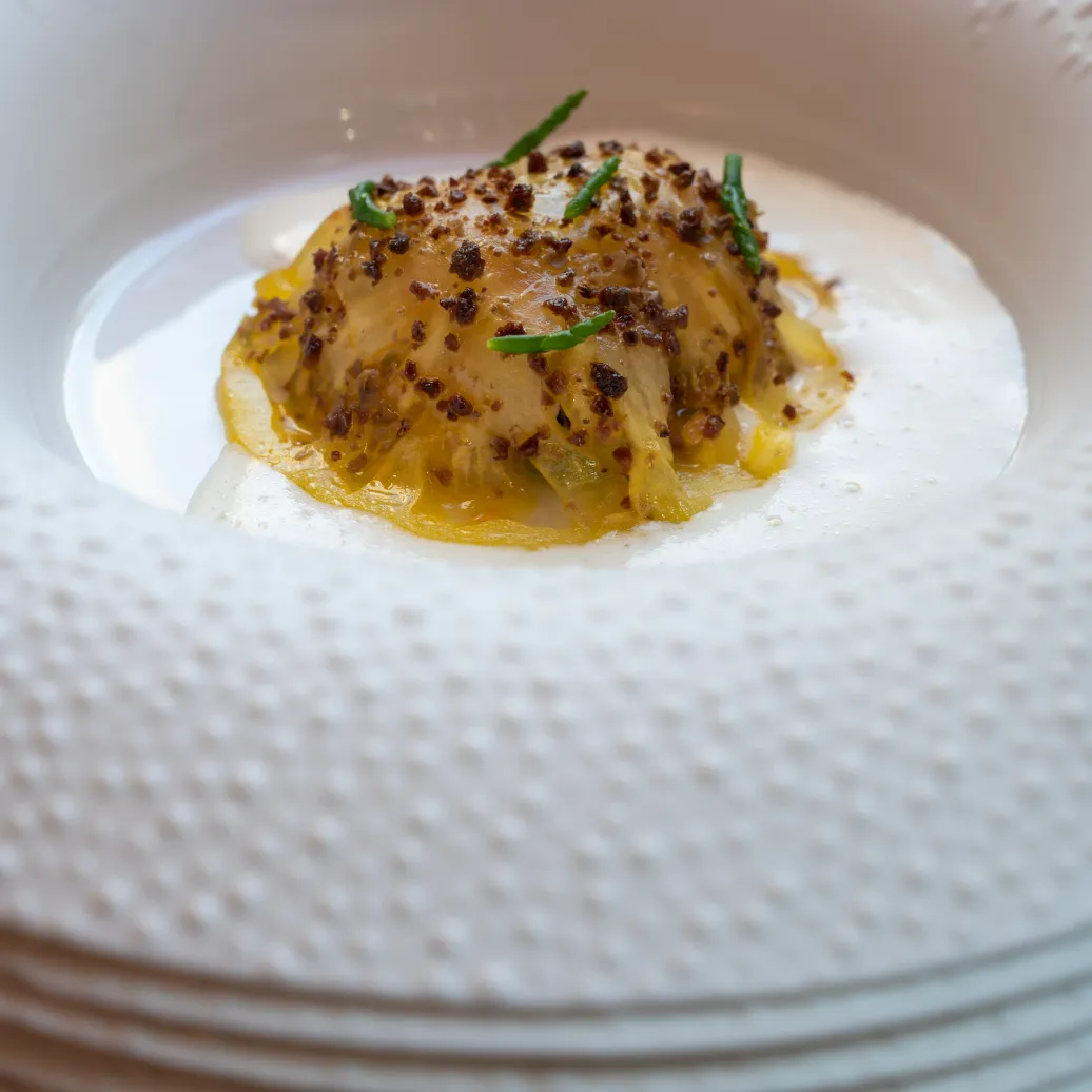 Un ravioli garni d'une préparation jaune, saupoudré de piment et de fines herbes, posé sur une assiette blanche empilée avec d'autres assiettes similaires