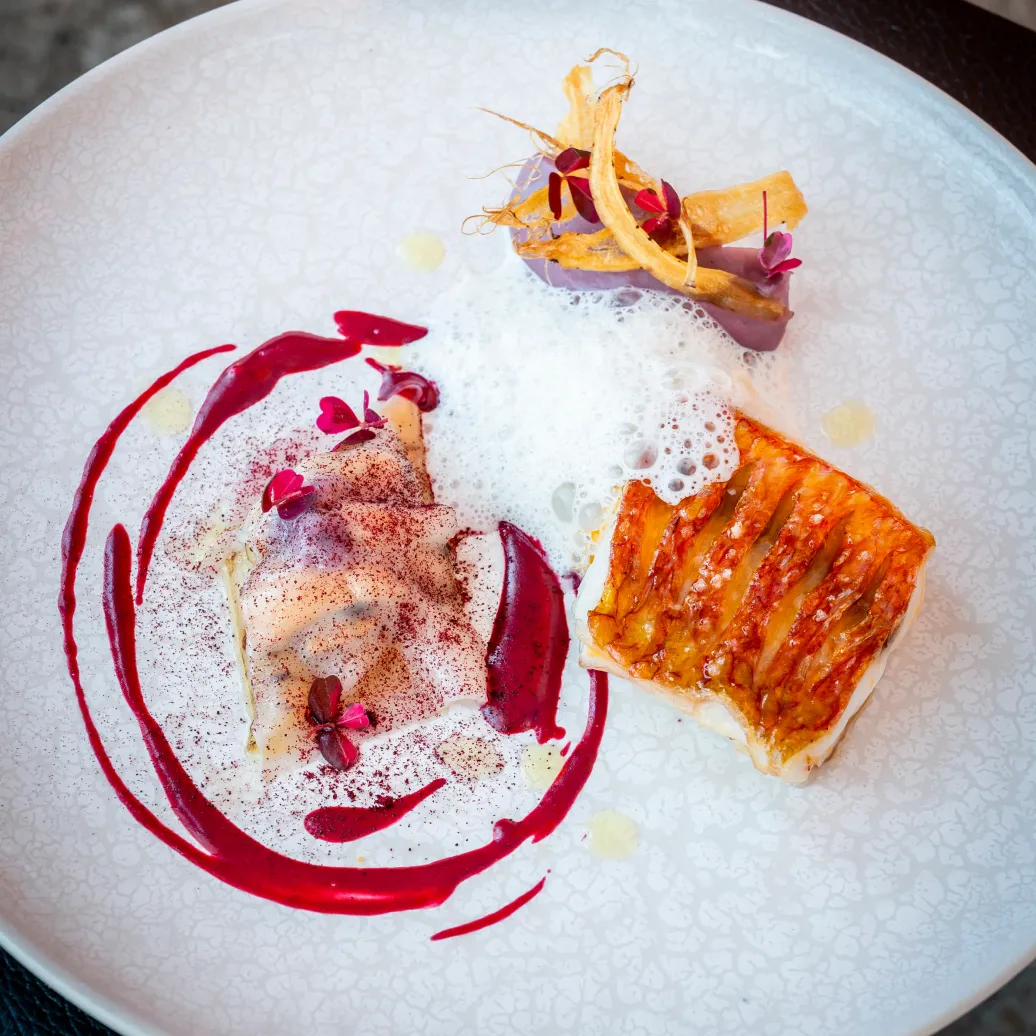 Assiette blanche avec deux portions de dessert, une sauce rouge et des garnitures variées