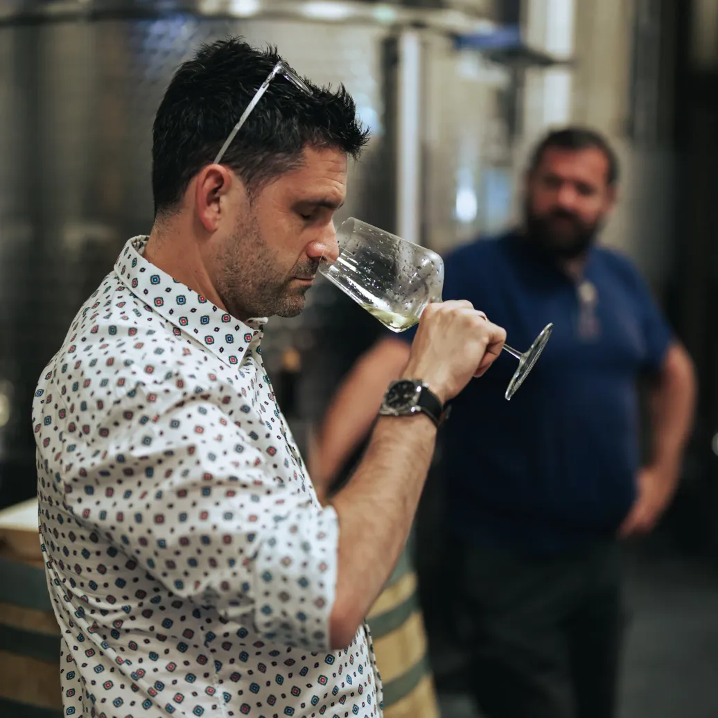 Un homme en chemise à motifs examine un verre de liquide transparent dans un environnement industriel avec des cuves en arrière-plan