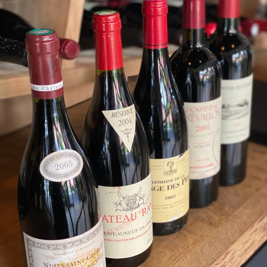Bouteilles de vin alignées sur une étagère en bois, avec des étiquettes visibles indiquant des millésimes et des noms de domaines