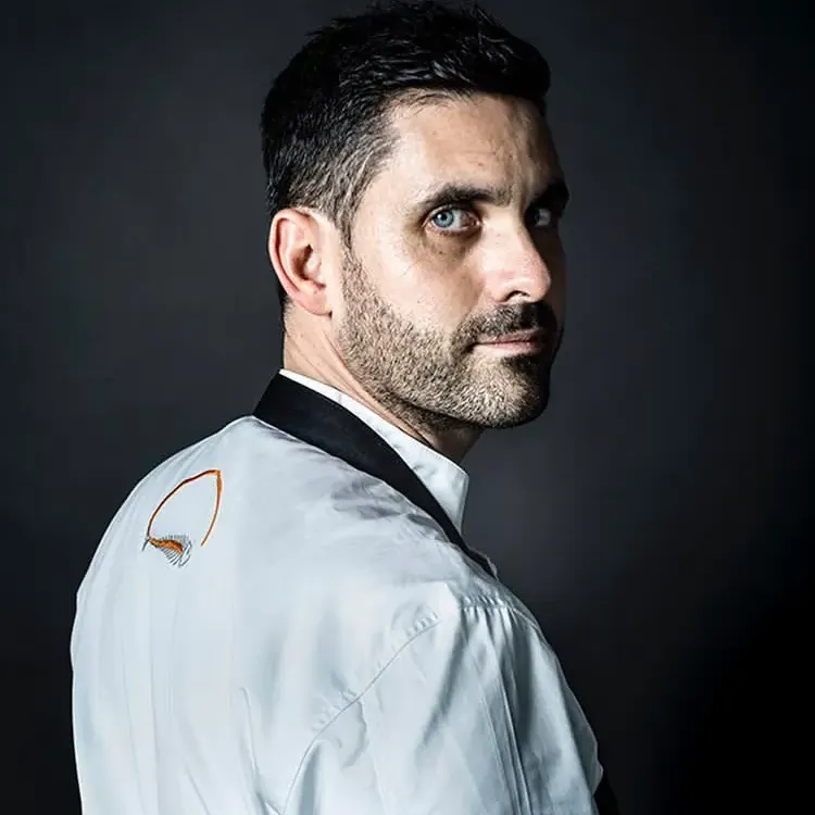 Homme en chemise blanche avec un logo sur l'épaule, regardant sur le côté, fond sombre