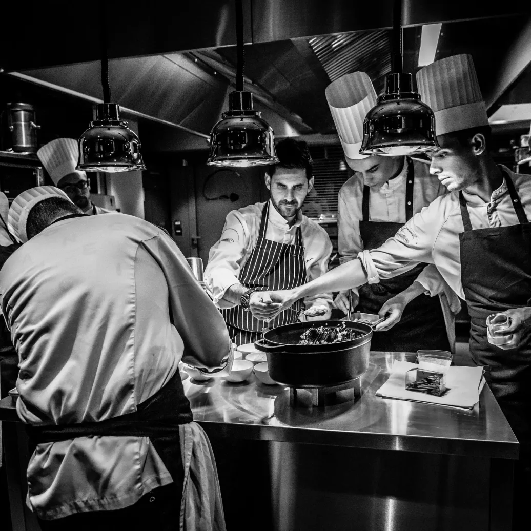Un groupe de chefs cuisiniers en toque et tablier travaille ensemble dans une cuisine professionnelle autour d'une grande marmite
