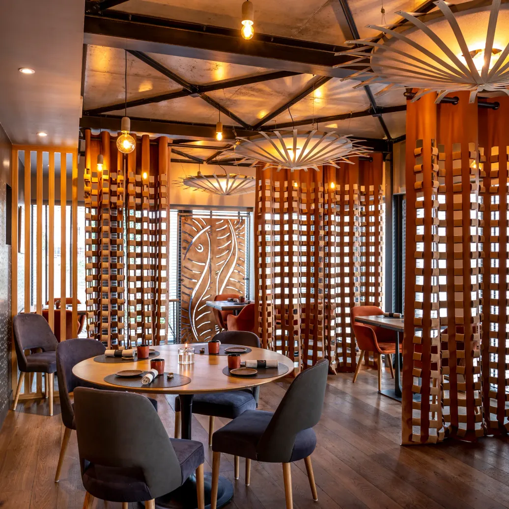 Restaurant intérieur avec des tables rondes, des chaises et des décorations en bois, éclairé par des lampes suspendues