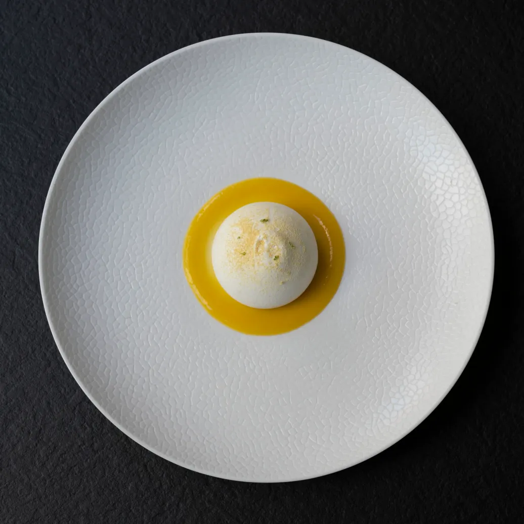 Une boule de glace saupoudrée de poudre verte dans une coupelle jaune sur une assiette blanche à motifs