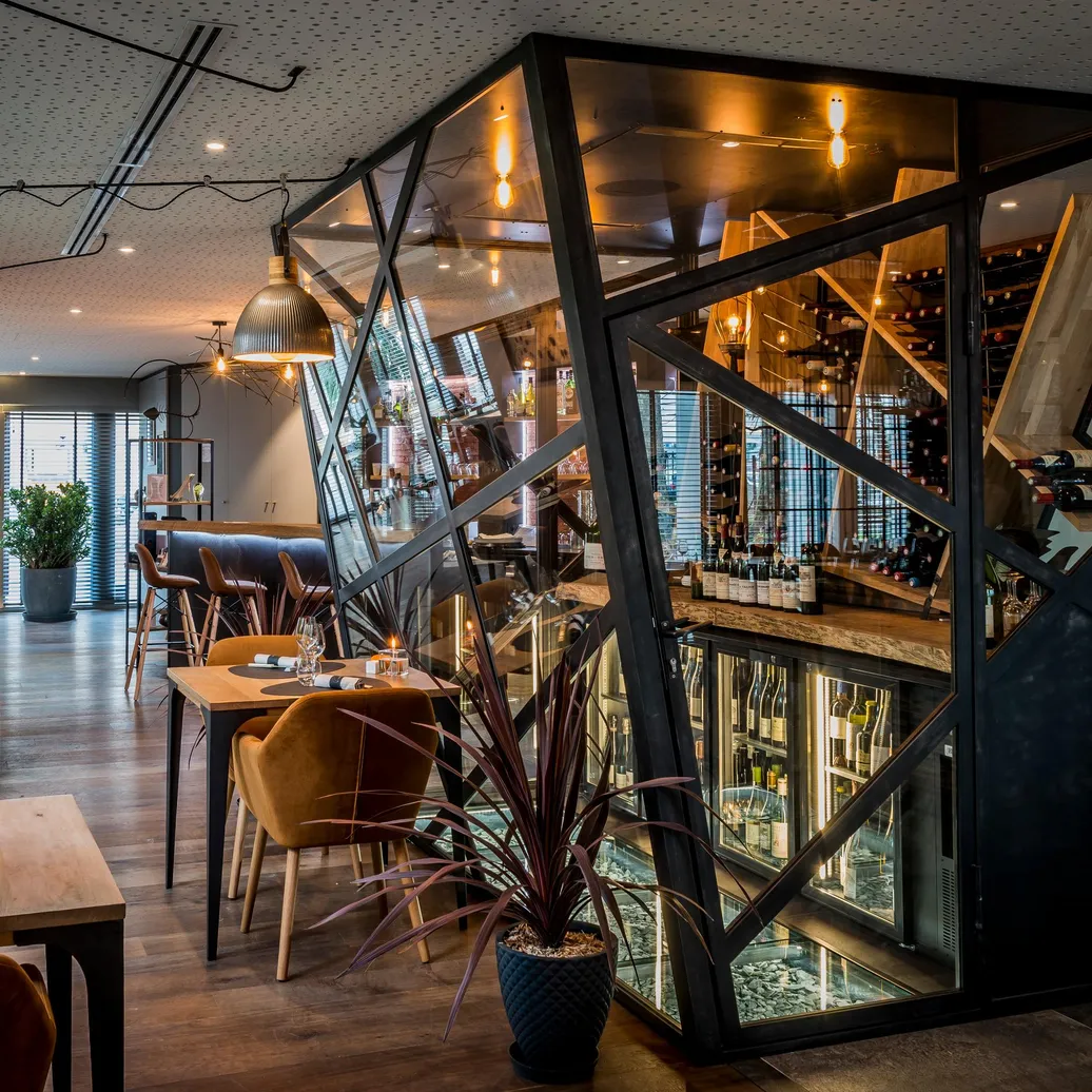 Restaurant moderne avec tables et chaises disposées dans une salle éclairée, miroir géométrique et plantes d'intérieur
