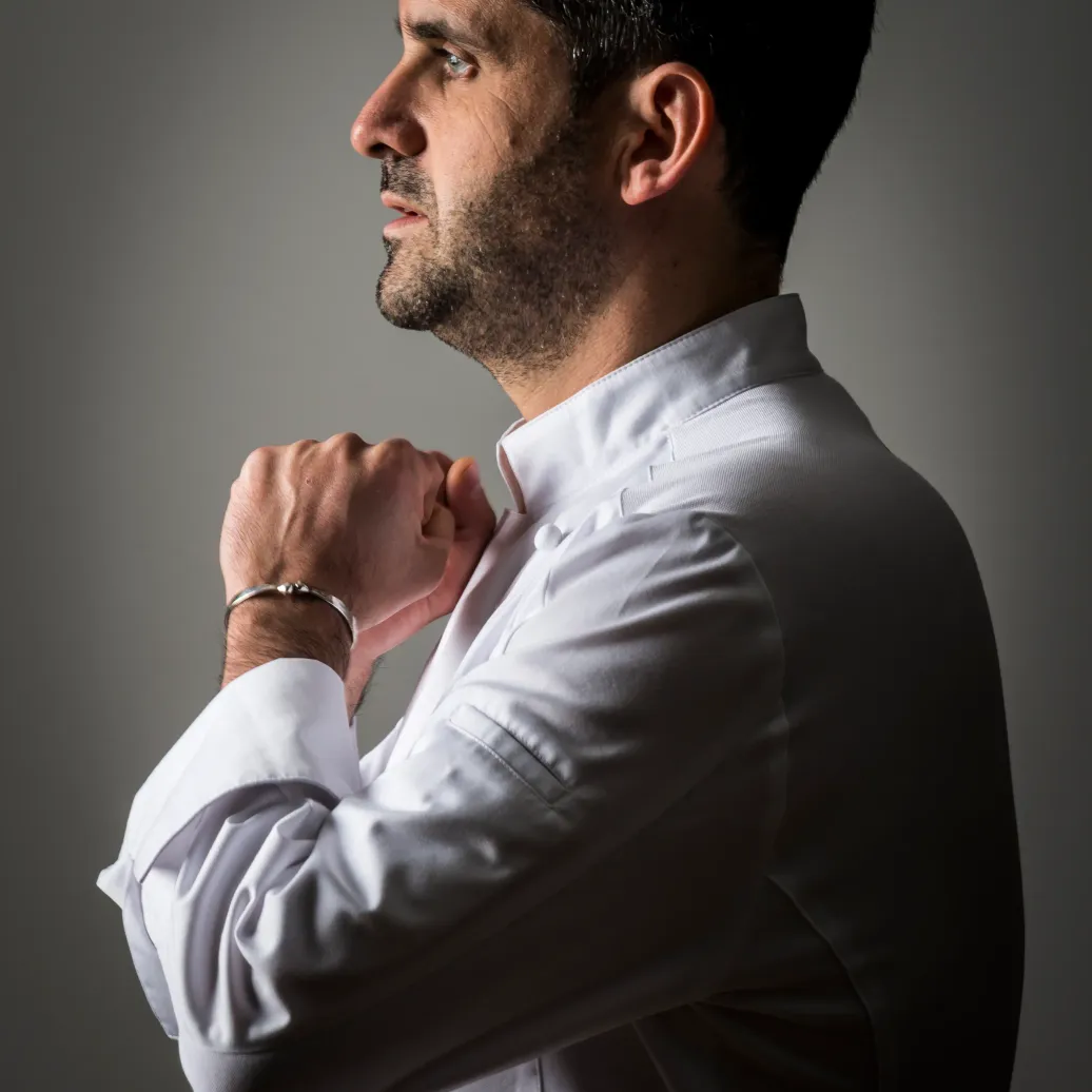 Homme en chemise blanche ajustant son col, profil droit, fond gris neutre