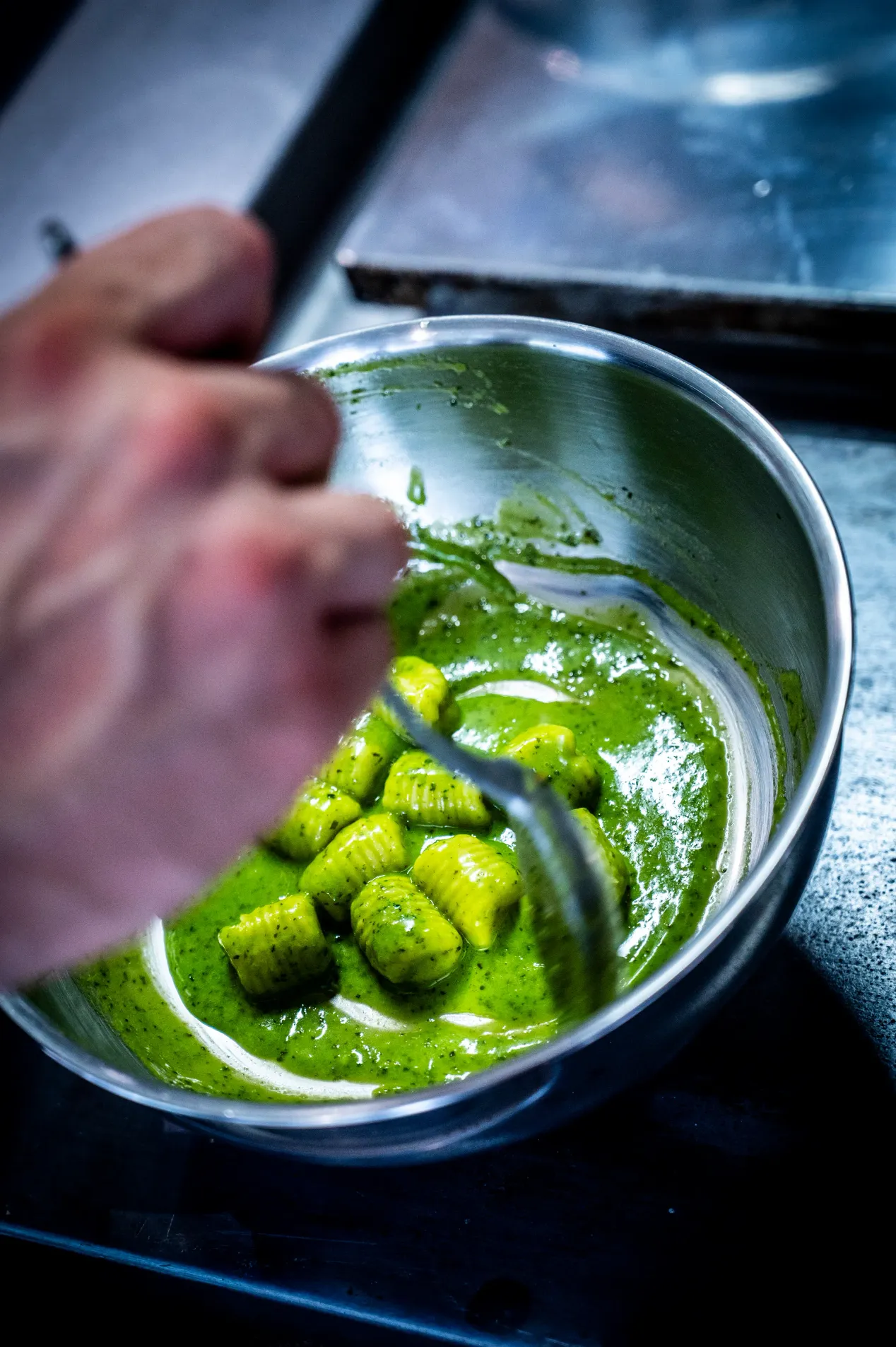 Une main remue une préparation verte dans une casserole avec une cuillère en bois
