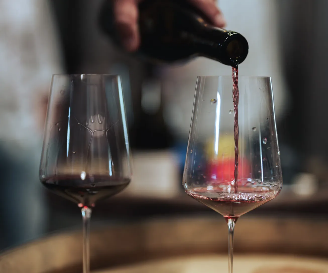 Une main verse du vin rouge dans un verre à pied posé sur une table en bois