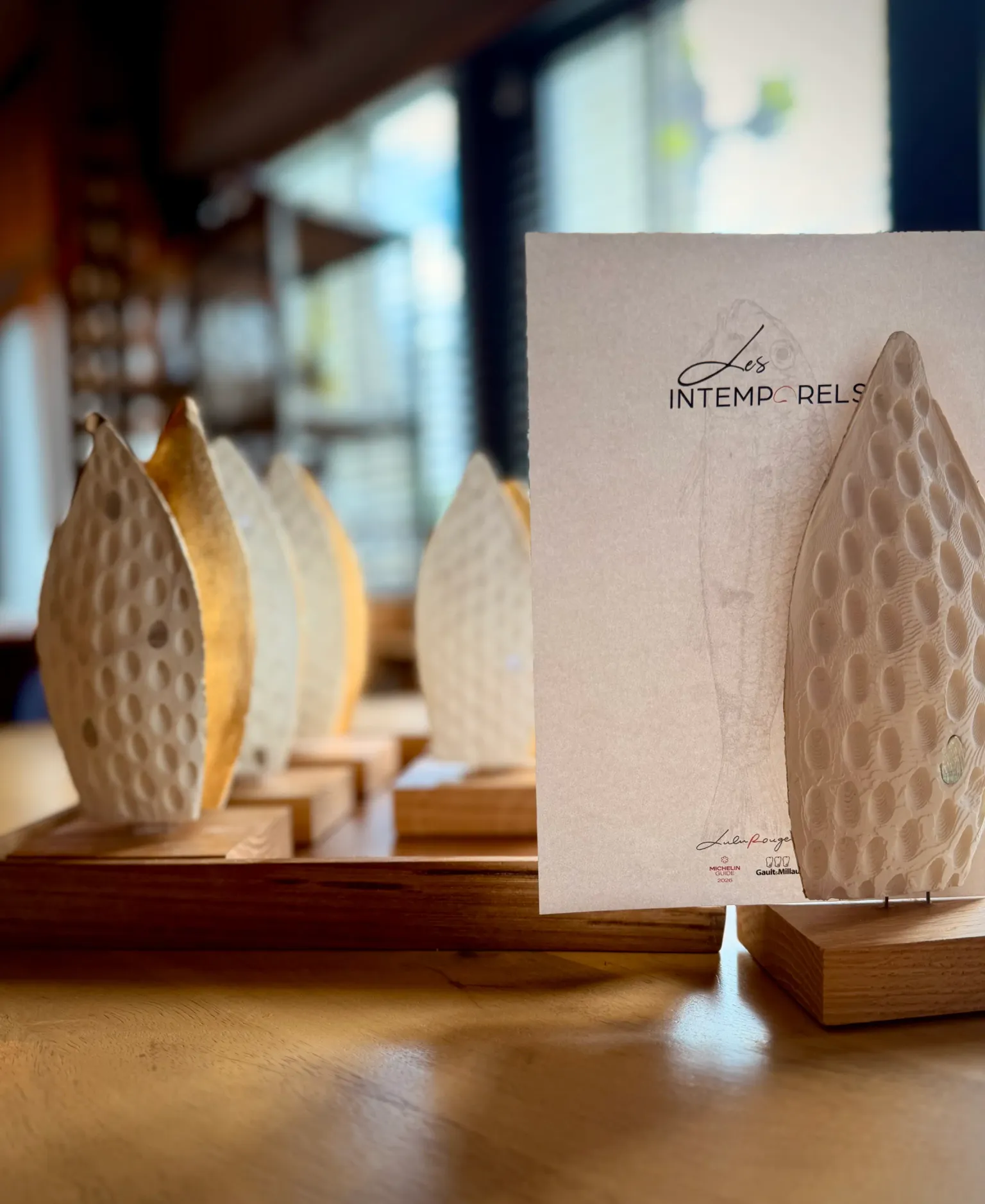 Des fromages en forme de feuilles sculptées sont disposés sur une table en bois avec une carte indiquant "Les Intemporels"