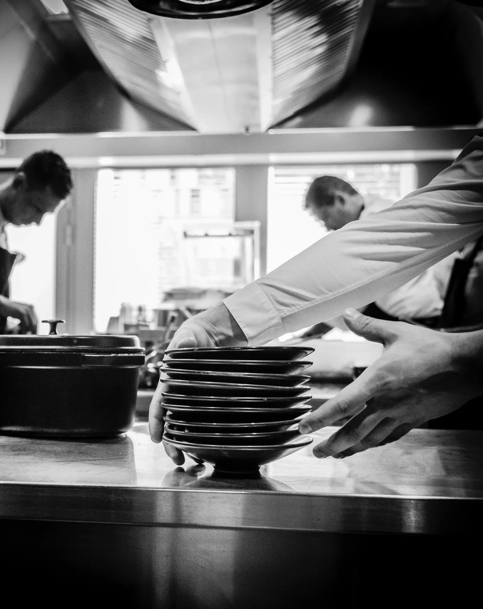 Des mains tiennent une pile d'assiettes dans une cuisine professionnelle, avec des personnes travaillant en arrière-plan