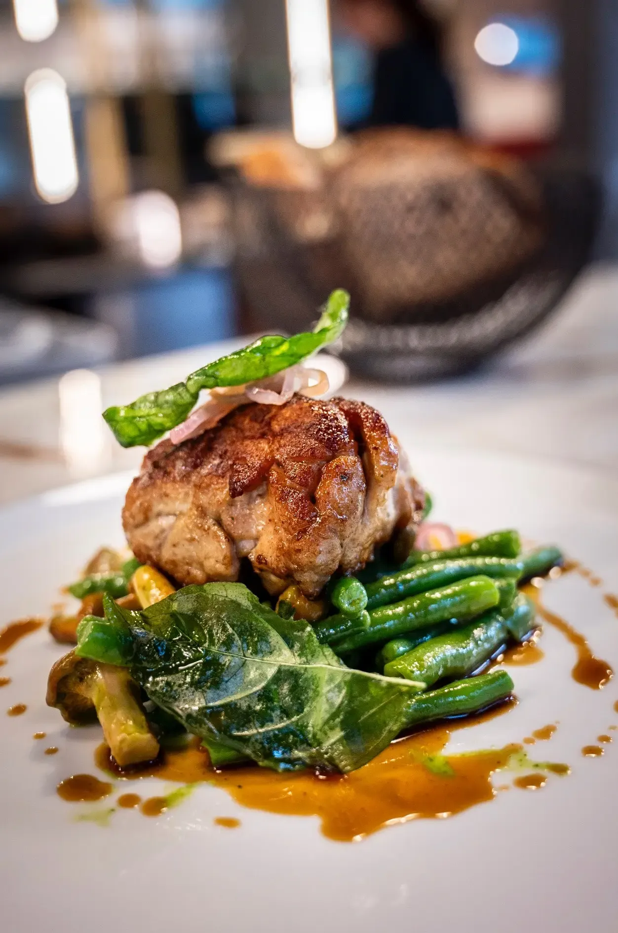 Un filet de bœuf grillé avec des haricots verts, des feuilles de basilic et une sauce au centre d'une assiette blanche