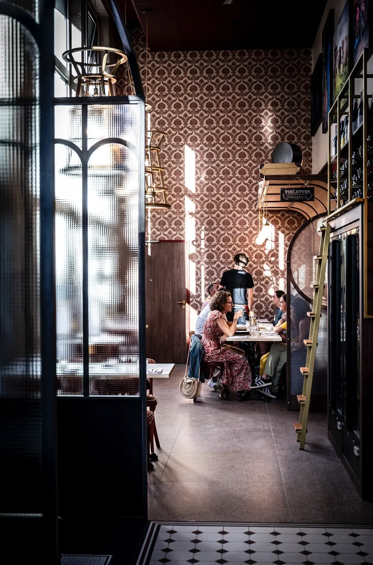 Un groupe de personnes est assis autour d'une table dans un restaurant à la décoration murale à motifs géométriques et aux lumières suspendues
