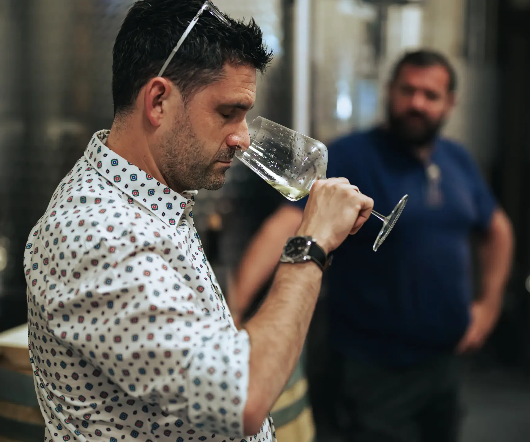 Un homme en chemise à motifs examine un verre de liquide transparent dans un environnement industriel avec des cuves en arrière-plan