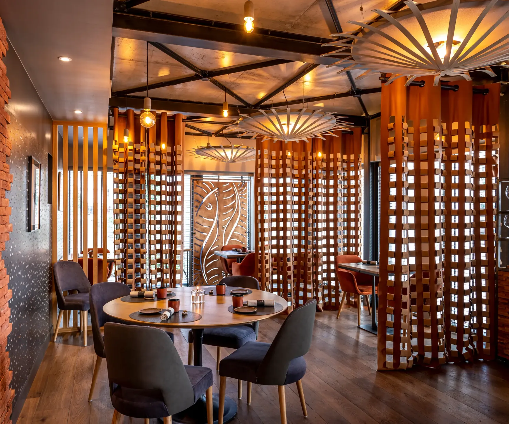 Restaurant intérieur avec des tables rondes, des chaises et des décorations en bois, éclairé par des lampes suspendues