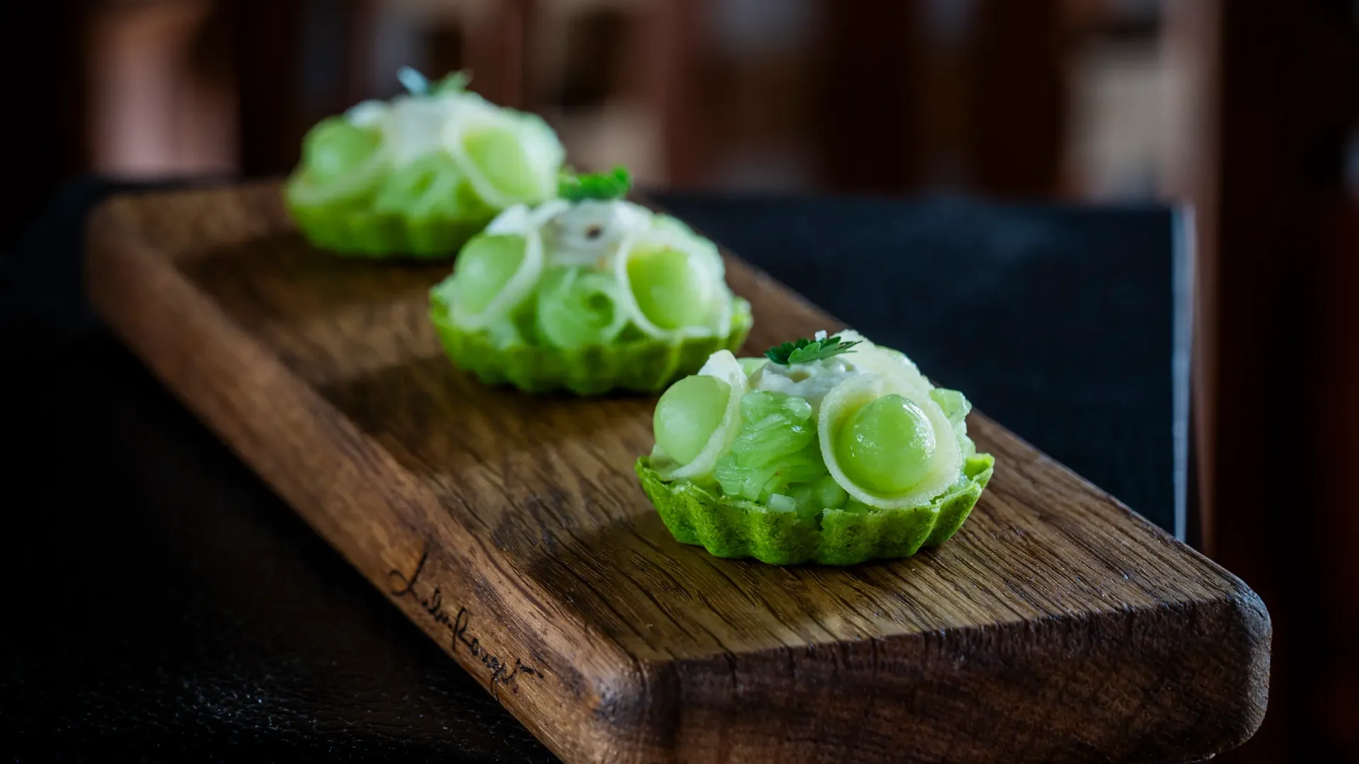 Trois boules de melon vert garnies de crème fraîche sur une planche en bois posée sur une table