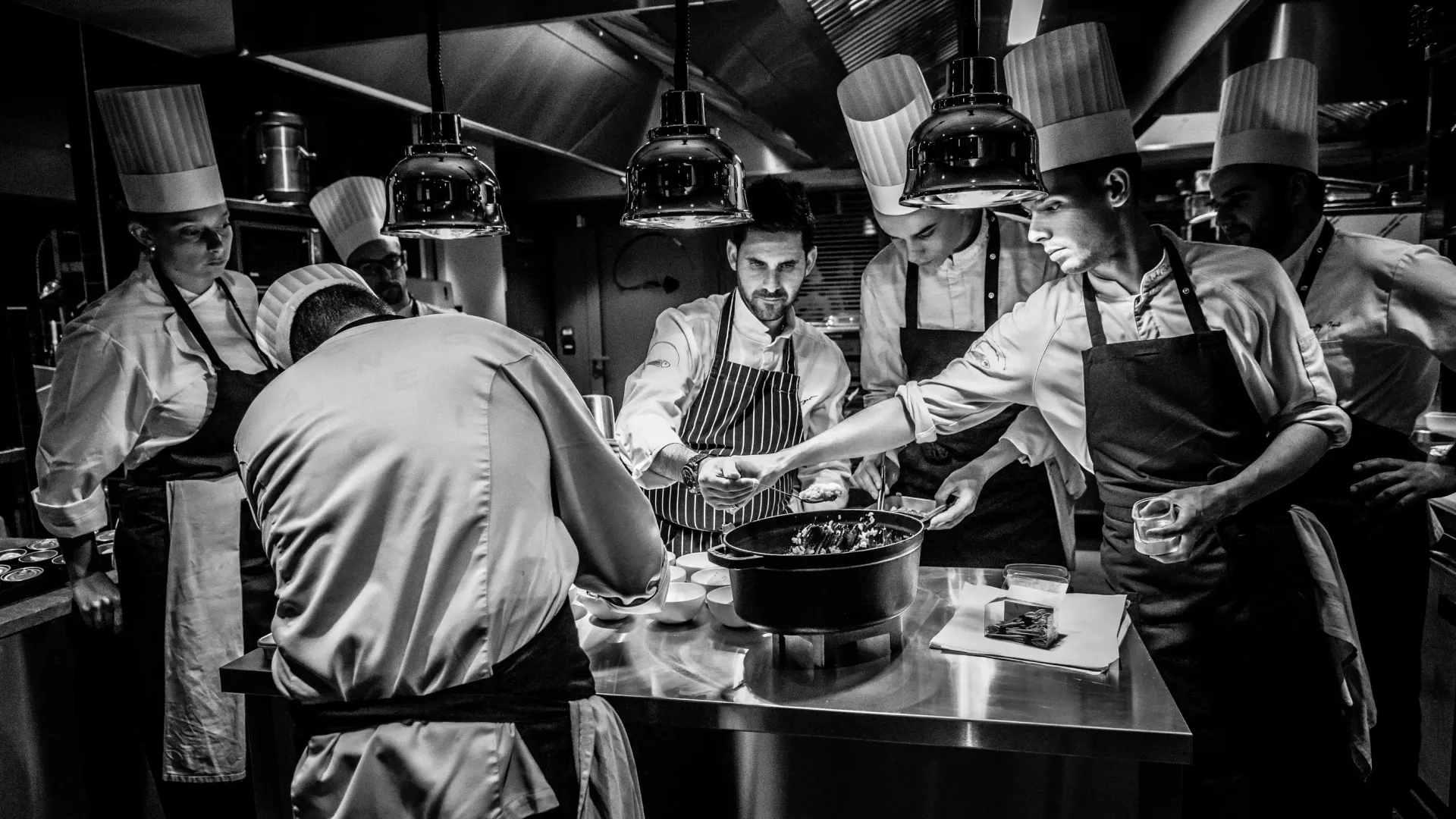 Un groupe de chefs cuisiniers en toque et tablier travaille ensemble dans une cuisine professionnelle autour d'une grande marmite