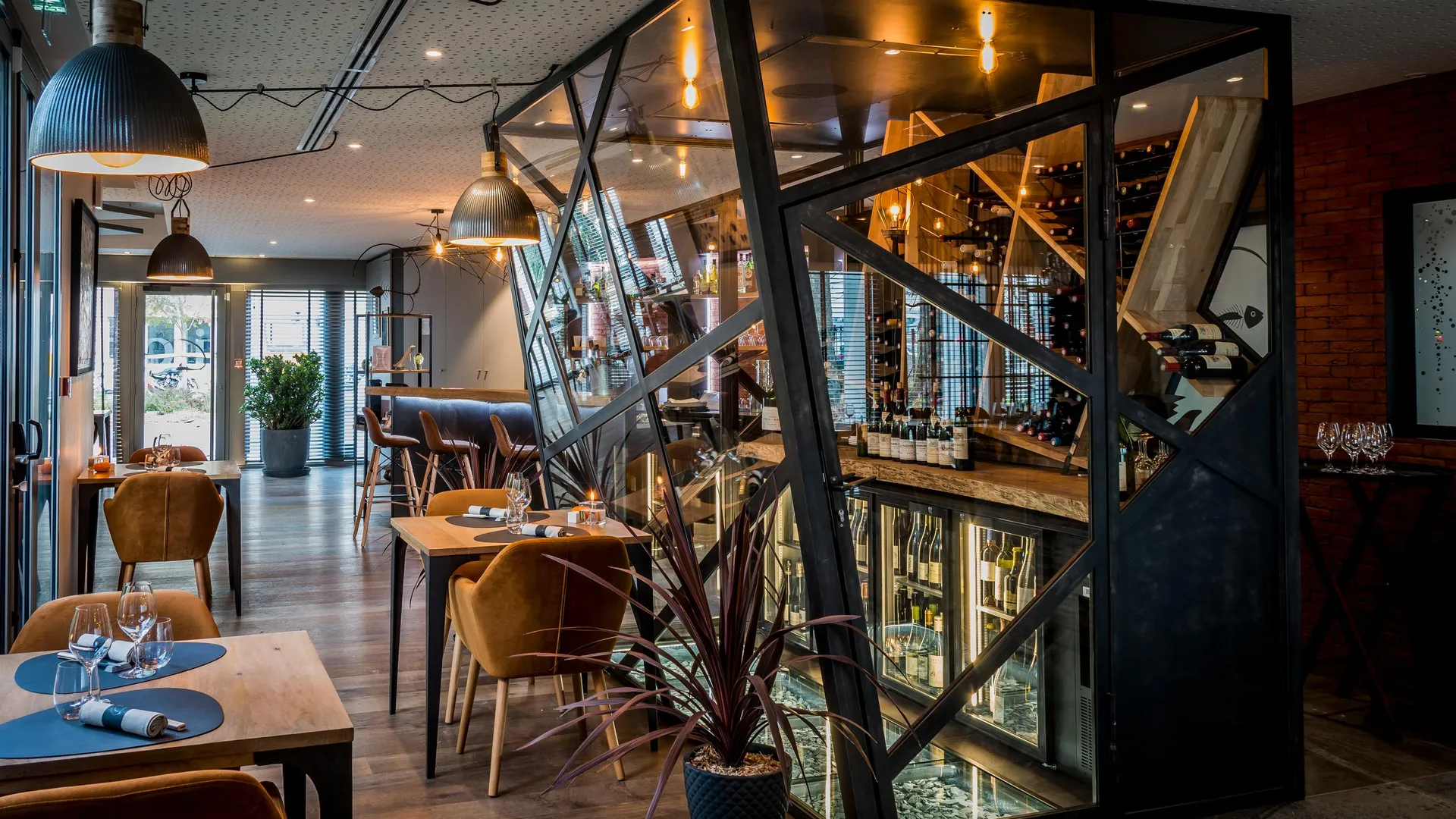 Restaurant moderne avec tables et chaises disposées dans une salle éclairée, miroir géométrique et plantes d'intérieur