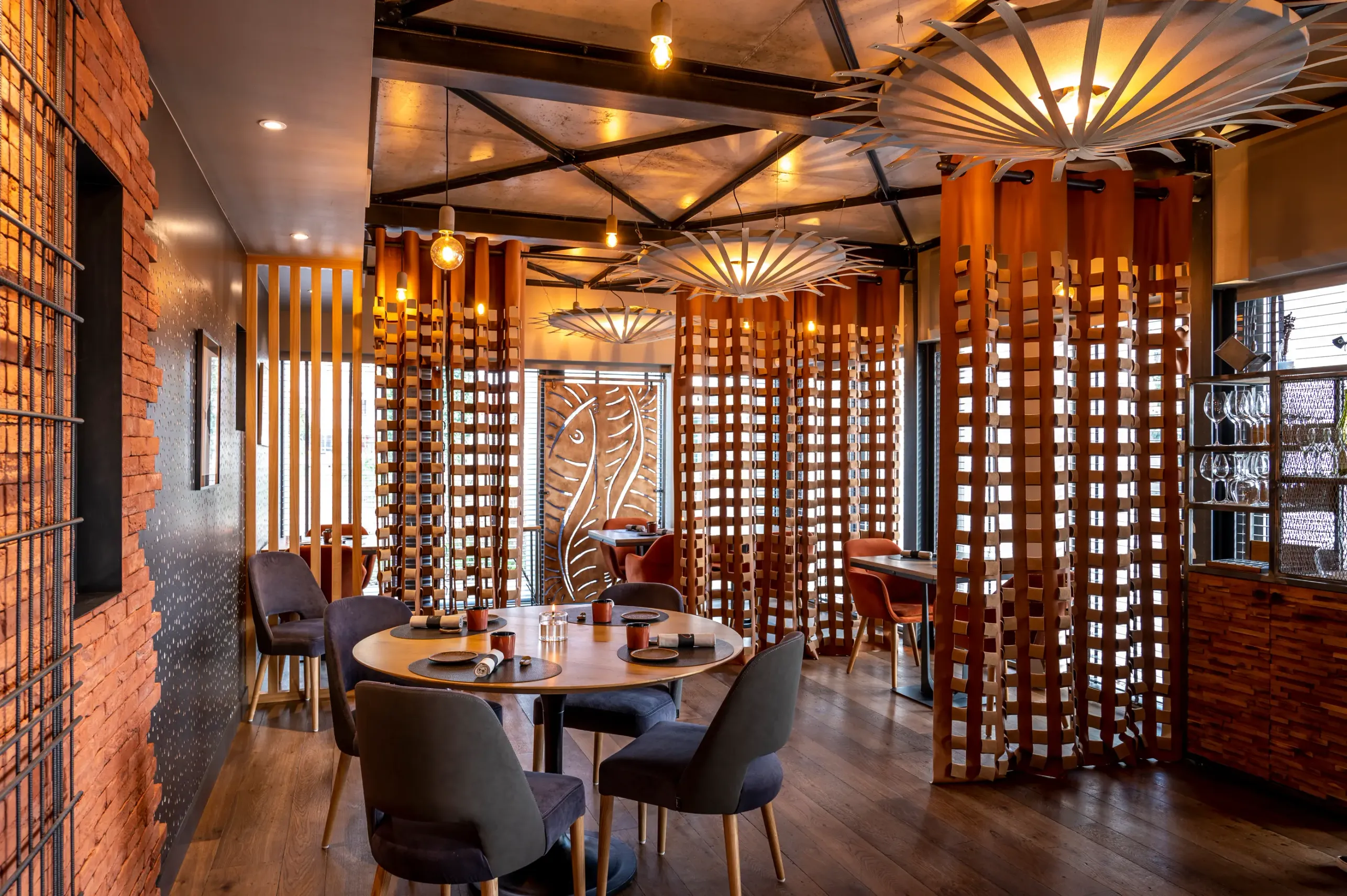 Restaurant intérieur avec des tables rondes, des chaises et des décorations en bois, éclairé par des lampes suspendues